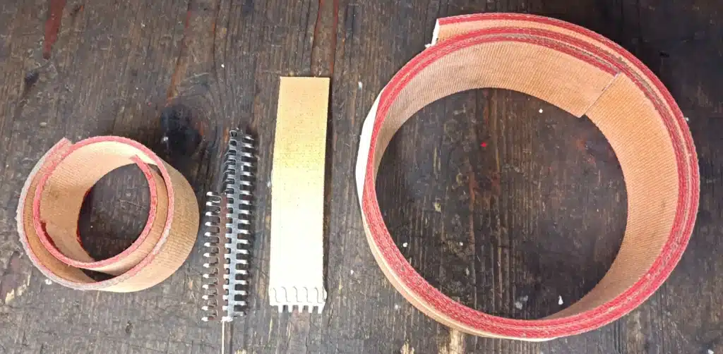 Courroies textiles beiges et rouges enroulées, attaches métalliques et section préparée sur bois. Matériel d'assemblage ou réparation.
