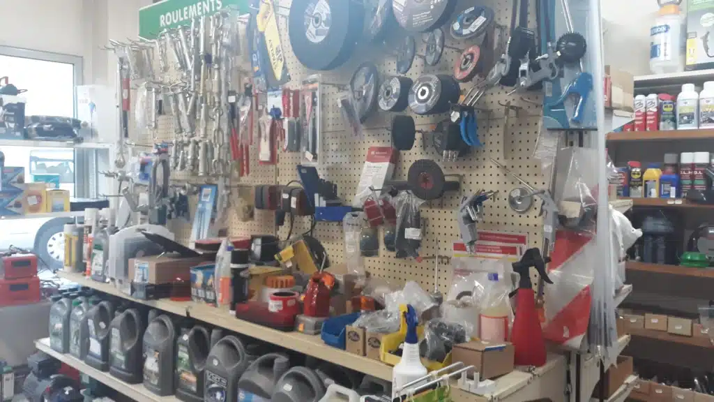 Allée de magasin de quincaillerie avec étagères d'huiles moteur, outils (Stanley), et pièces sur panneau perforé sous 'ROULEMENTS'.