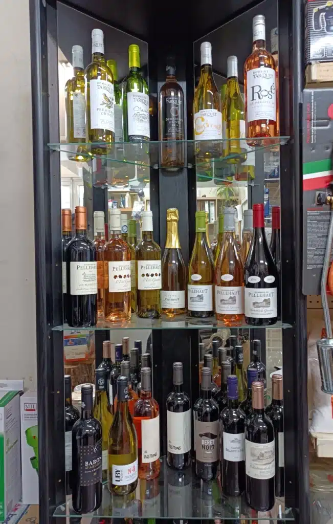 Collection de vins rouges, rosés et blancs (Tariquet, Pellehaut, UBY, Baron d'Ardeuil) sur étagères d'un meuble sombre avec reflets.